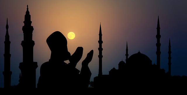 Silueta modliacej sa osoby počas západu slnka pri siluetách veží
